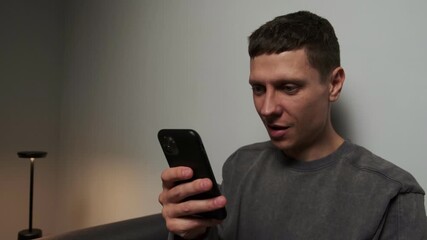 Emotional reaction to smartphone. Close up young man at home in minimalist room showing surprise after seeing content