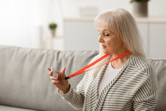 Senior People Support Concept. Portrait of old woman holding and looking at red alert button for emergency while staying home alone, closeup, free copy space. Medical equipment for help