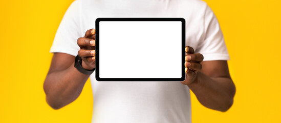Mobile app, good service, ad and website recommendation. African american millennial guy in white t-shirt showing digital tablet with blank screen, isolated on orange background, studio shot, cropped