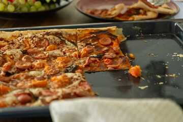 Pizza with pepperoni and sausages is cut in half and spread on a black frying pan. Pizza is served on the table.delicious dinner for the whole family, fast food, junk food.