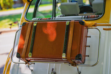 Close-up of vintage brown suitcase attached to car luggage rack with leather straps and umbrella....