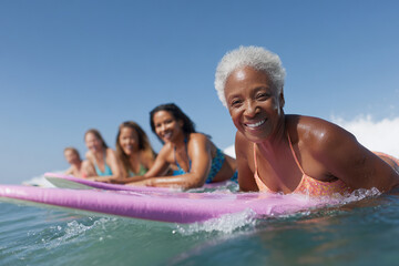 Group of women of various ages smiling and paddling out on surfboards in the ocean, enjoying a day of surfing in a tropical location.