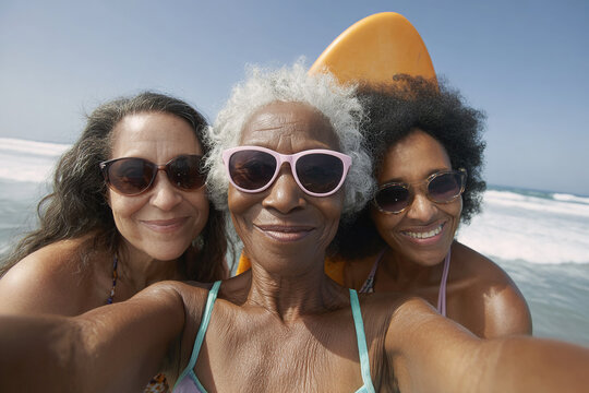 Three generations of women smiling at the beach. Wearing sunglasses, a surfboard is behind them in this selfie on the ocean shore. - Powered by Adobe