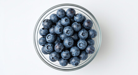 Overhead shot of fresh blueberries in a clear glass bowl on a white surface in bright light