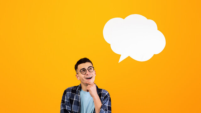 Thoughtful young guy looking at empty speech bubble over orange studio background, mockup for design. Handsome millennial man with blank word cloud, space for your ad