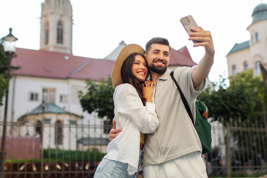 Romantic couple walking on the city street embracing and taking selfie photo on smartphone while sightseeing on trip