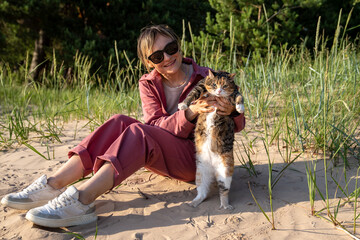 Funny grumpy protesting cat hanging in owner hands wanting to go home instead of walking on beach....
