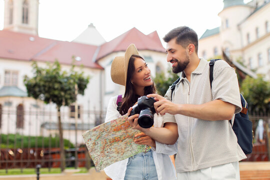 Happy couple of tourists walking in city while sightseeing the town and taking photos on camera, woman holding map and looking at taken pictures