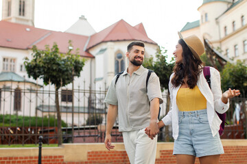 Happy young man and woman talking while walking along street in beautiful European city outdoors,...