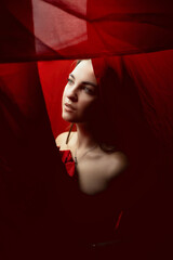 Model gazing thoughtfully through sheer red fabric in an artistic studio setting during the daytime