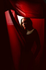 Model poses gracefully behind red curtain, creating a dramatic and intimate atmosphere in a softly...