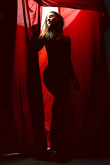 Woman in silhouette standing behind red curtain during a dramatic lighting setup in a studio
