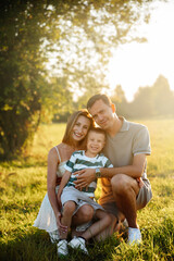 A family of three shares joyful moments in a lush green field under the warm sunlight, creating...
