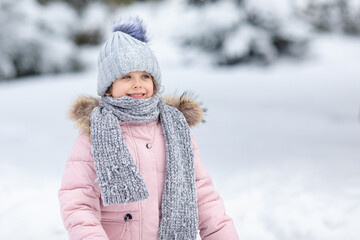 Winter portrait with copy space happy excited little girl in warm clothes playing in winter park and joyfully laughing on sunny snowy day. Fun outdoor activities for children in wintertime.