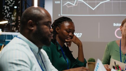 Diverse project team shares analytics reports during advisory board event after hours, reviewing...