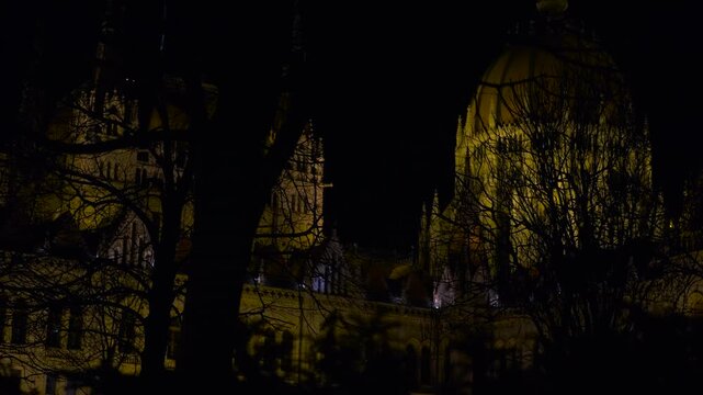 Hungarian Parliament Building at Night. Light progressively illuminates the hungarian parliament building in budapest at night, revealing its architectural details behind dark silhouettes of trees