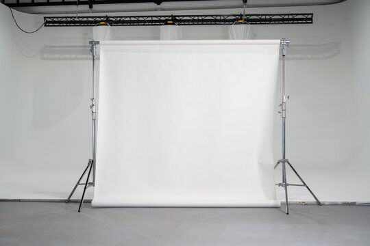 Empty professional photo studio setup with seamless white paper backdrop on stands, neutral background for portraits, product photography, or fashion shoots, symbolizing creativity, preparation