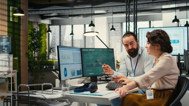 Business partners engaging in a discussion about financial forecasting and data insights, cheerful teamwork in a modern workspace. Man and woman ensuring goals achievement.