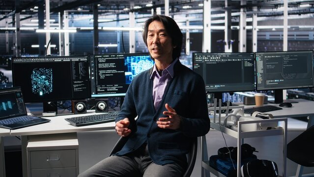 Data center admin waving hand, filming presentation tour, showcasing mainframes and AI technology. Upbeat Asian man in server room presenting artificial intelligence neural networks tech, camera A