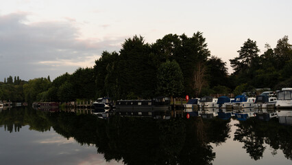Fototapeta premium A serene scene of boats moored near a historic lock and dam architecture. Calm waters reflect the structures and vessels, capturing a peaceful moment of nautical life and industrial heritage.