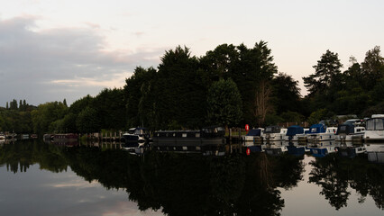 Fototapeta premium A serene scene of boats moored near a historic lock and dam architecture. Calm waters reflect the structures and vessels, capturing a peaceful moment of nautical life and industrial heritage.