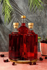 Homemade strong cherry cider in bottles and glasses on elegant background, still life with alcoholic drinks and fresh cherries, home winemaking concept, minimalist banner for bar