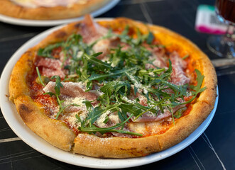 A mouth-watering Italian pizza with prosciutto, arugula, and parmesan cheese on a white plate