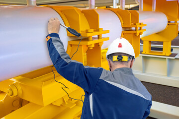 Engineer in hard hat performs ultrasonic testing on industrial pipeline using inspection equipment....
