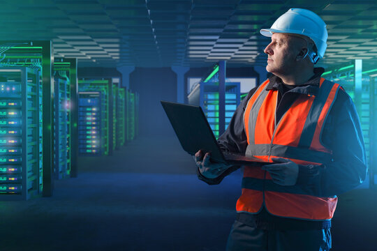 Engineer in safety vest and helmet with laptop inspecting modern data center with glowing server racks, monitoring IT infrastructure, cybersecurity, networking, technology.