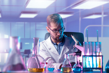 Scientist in laboratory coat working with microscope and colorful chemical liquids in glassware,...