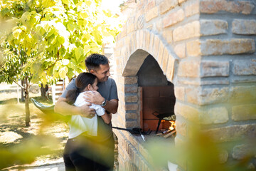 Father embracing daughter while cooking in outdoor brick oven