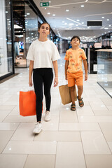 Obraz premium Teen girl and little boy walking in shopping mall with shopping bags