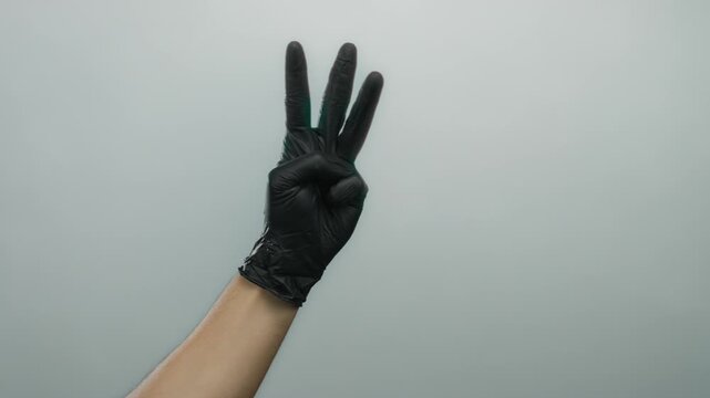 Hand in black glove showing number three against white background representing gesture communication isolate.