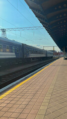 Train passing through a busy station on a sunny day with clear skies and platform activity