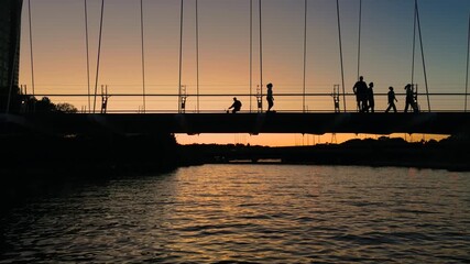Silhouettes of pedestrians on the Humber River bridge against a warm sunset - Powered by Adobe