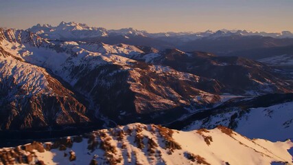 Flying over mountains, moving through rough and high reach mountain peaks covered in snow with clouds and upcoming sunlight, nature landscape view