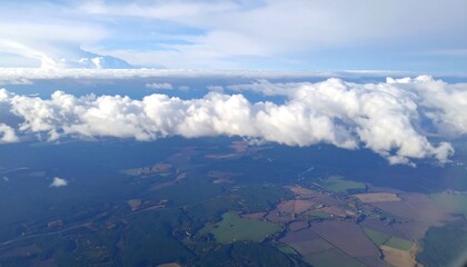 High-altitude view reveals a vast landscape, with fluffy white clouds cascading over fields of varying hues, creating a serene and expansive panorama.