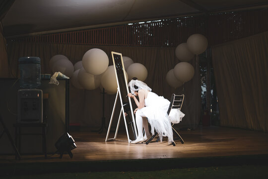 A girl in a wedding dress is leaning over the mirror to put on her makeup. Dark background of the dressing room and baloons in the background. High quality photo