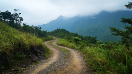 Winding dirt road through lush mountain landscape, hazy sky