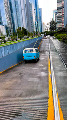 Fototapeta premium Vintage turquoise van driving into an urban modern cityscape after rain