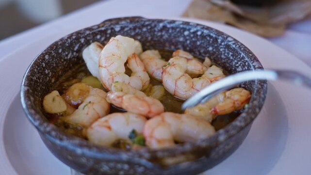 Shrimp dish served in a rustic bowl at a mediterranean restaurant, featuring a delicious seafood meal indoors on a table with garlic and a fork for dining.