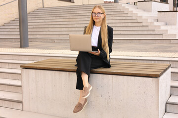 Young woman sitting on a wooden bench with a laptop on her lap. 