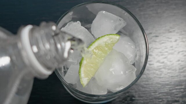 Pour tonic in glass with lime slice and ice 
