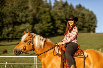 Obraz premium Young woman riding Haflinger horse on ranch with cattle in background