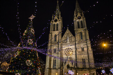 The festive lights of Náměstí Míru glow warmly, highlighting St. Ludmila Basilica beside a...