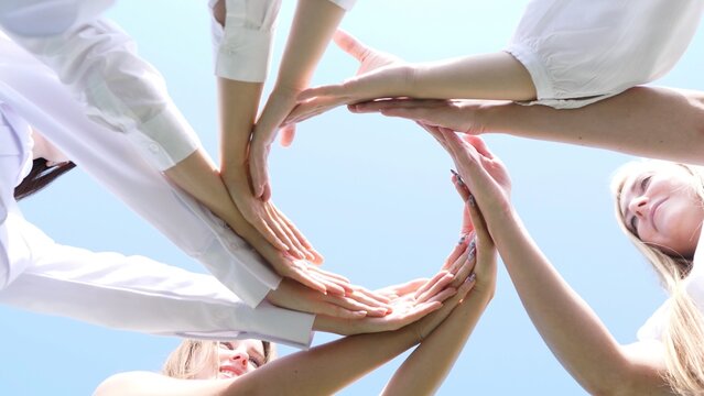 Various diverse hands have come together, united against a vivid, bright sky that represents unity and teamwork