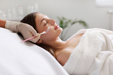 Beautician applying facial mask on young female face, lady receiving skin care treatment,...