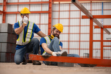 Construction worker injured in workplace accident, holding foot in pain while colleague calls for...