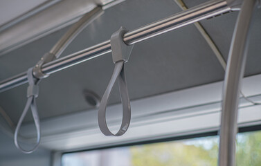 Close-up of hand straps inside public transportation. The gray loops attached to metal bars provide passengers with stability and safety while standing on a bus or tram during travel. Selective focus.