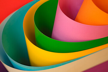 Close-up of colorful sheets of paper rolled into curves. Creating a vibrant abstract composition. The bright tones of pink, green, yellow, orange and blue form a playful and artistic visual.